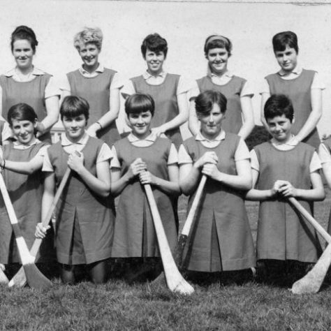 Black and white team photo of women on a field holding bats